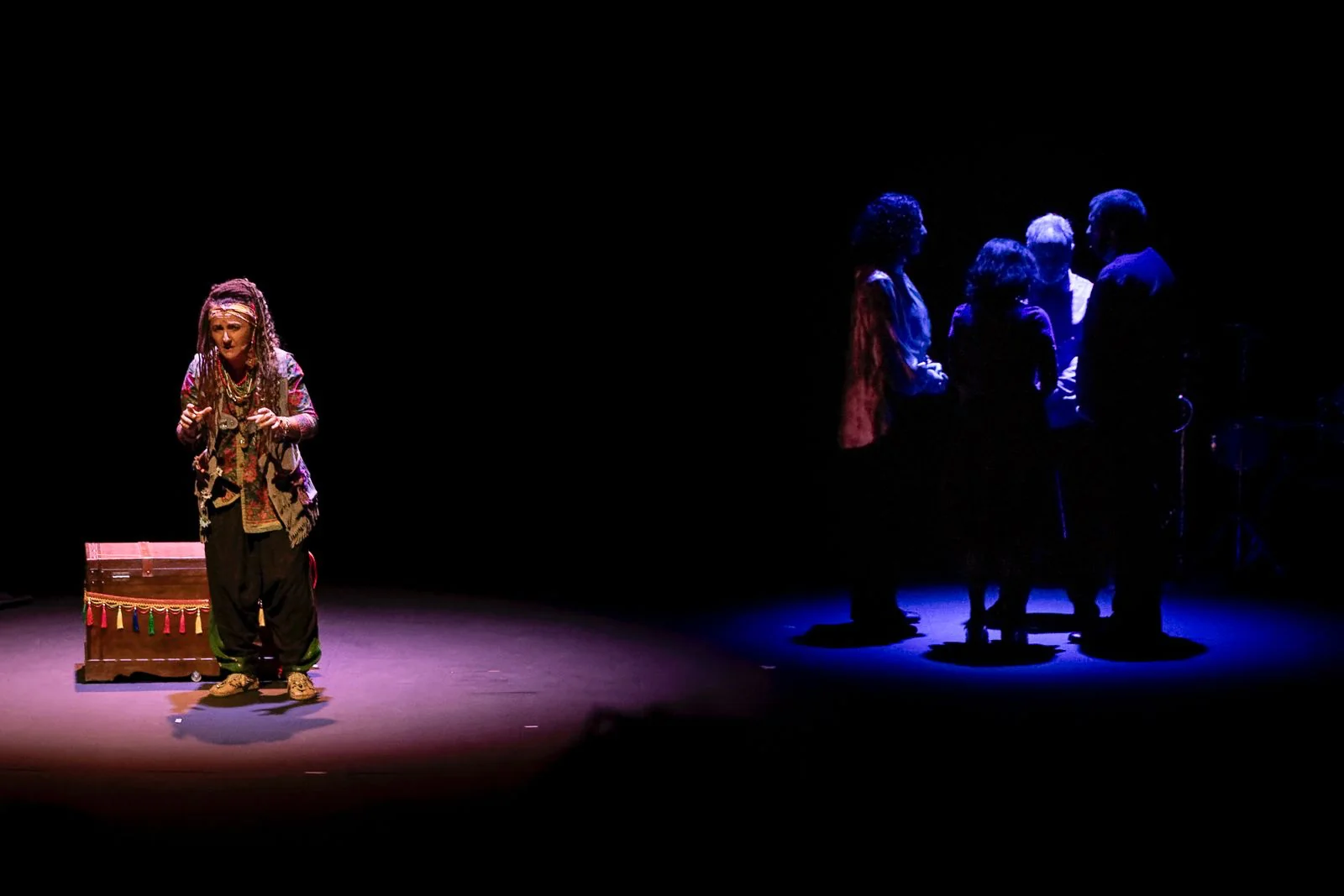 Kala actúa junto al baúl mientras el elenco permanece en penumbra