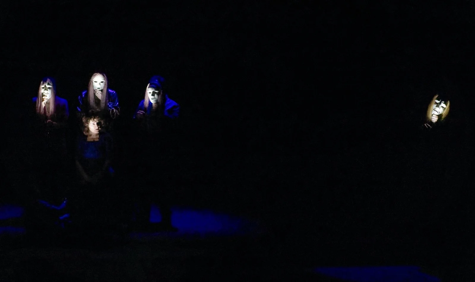El elenco interpreta una escena iluminada con máscaras